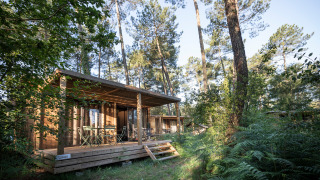 Buitenaanzicht van Chalet Evasion in Huttopia Landes Sud, Frankrijk, omgeven door een weelderig groen bos.