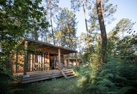 Buitenaanzicht van Chalet Evasion in Huttopia Landes Sud, Frankrijk, omgeven door een weelderig groen bos.