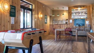 Acogedora sala común en Huttopia Landes Sud con futbolín, decoración de madera y barra de bebidas.