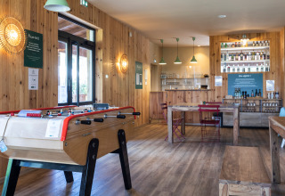 Moderne fællesrum i Huttopia Landes Sud med bordfodboldbord, træmøbler og hyggelig bar.