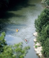 Dos personas navegan en kayak por un río rodeado de árboles en un parque vacacional con glamping.