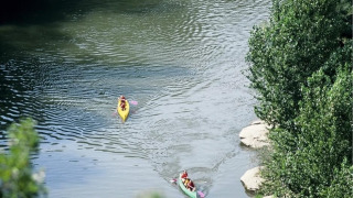 Dos personas navegan en kayak por un río rodeado de árboles en un parque vacacional con glamping.