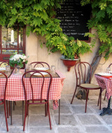 Acogedor café al aire libre con manteles a cuadros rojos y blancos y plantas verdes exuberantes.