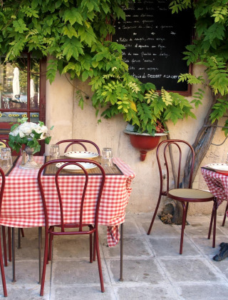 Acogedor café al aire libre con manteles a cuadros rojos y blancos y plantas verdes exuberantes.