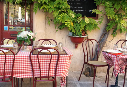 Charming outdoor café with red and white checkered tablecloths, vintage chairs, and lush green foliage.