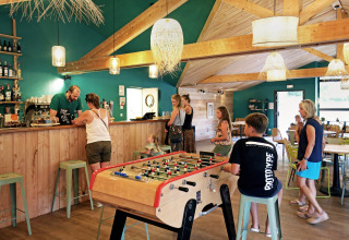 Folk i afslappet ferieatmosfære på Huttopia Etang de Fouché, Bourgogne, med bordfodbold og café.
