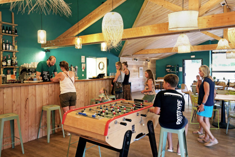 Personas disfrutan de un ambiente vacacional relajado en Huttopia Etang de Fouché, Francia, con futbolín y cafetería.