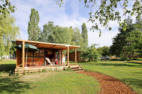 Cabaña de madera con porche cubierto y mobiliario de exterior en Huttopia Etang de Fouché, Borgoña, Francia