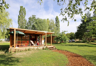 Træhytte med overdækket terrasse og havemøbler i grønt område på Huttopia Etang de Fouché, Bourgogne, Frankrig