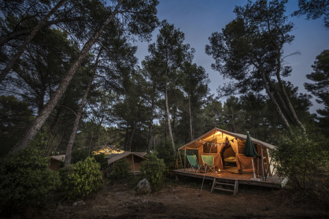 Vista nocturna de la tienda safari Bungalow Classic en Huttopia Fontvieille, Francia, rodeada de pinos altos.