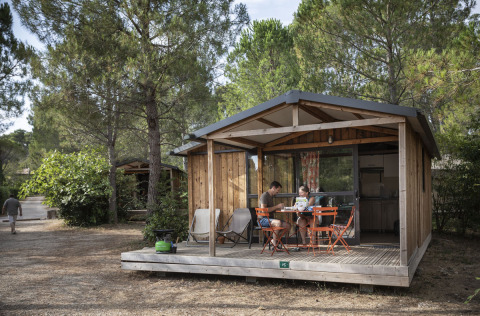 Gezin op het terras van een houten hut bij Huttopia Fontvieille in Provence-Alpes-Côte d’Azur, Frankrijk.