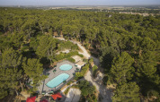 Luftfoto af Huttopia Fontvieille feriepark i Provence-Alpes-Côte d’Azur, Frankrig, omgivet af fyrretræer.