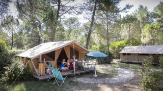 Safaritent bungalow in het bos bij Huttopia Fontvieille in Frankrijk met mensen die buiten ontspannen.