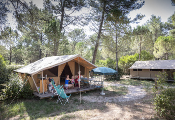Safari-bungalowtelt i skoven ved Huttopia Fontvieille i Frankrig med folk, der slapper af udenfor.