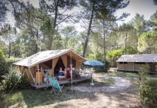 Tienda tipo bungalow de safari en el bosque de Huttopia Fontvieille, Francia, con personas relajándose.