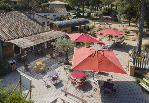 Sonnige Terrasse mit roten Sonnenschirmen und bunten Stühlen bei Huttopia Fontvieille, Provence.