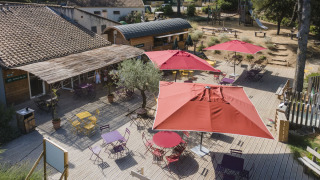 Terraza al aire libre con sombrillas rojas y sillas coloridas en Huttopia Fontvieille, Provenza, Francia.