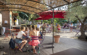 Udendørs spisning på en solrig terrasse med folk, træer og parasoller i Huttopia Fontvieille, Provence.
