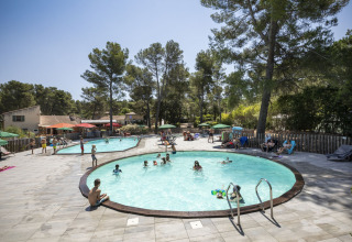 Families genieten aan het zwembad van Huttopia Fontvieille vakantiepark, omgeven door bomen in Zuid-Frankrijk.