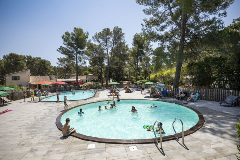 Children and families enjoy the outdoor pool and relax by the trees at Huttopia Fontvieille holiday park, France.