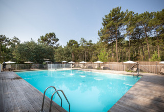 Udendørs swimmingpool omgivet af træterrasse og liggestole i ferieparken Huttopia Lac de Carcans, Frankrig.