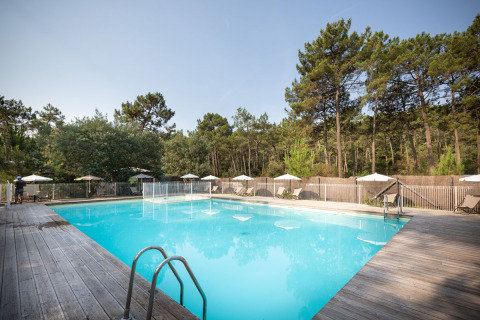 Piscine extérieure avec terrasse en bois et transats au parc de vacances Huttopia Lac de Carcans, France.