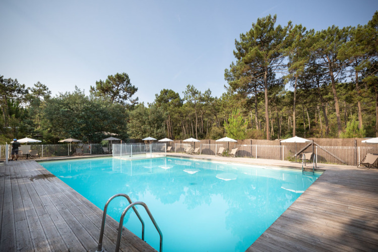 Outdoor swimming pool with wooden deck and lounge chairs at Huttopia Lac de Carcans holiday park in France.
