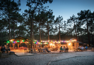 Evening at Huttopia Lac de Carcans holiday park, with string lights, wooden tables, and forest in France.