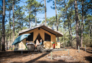 Familia sentada frente a una tienda safari en un bosque de pinos en Huttopia Lac de Carcans, Nouvelle-Aquitaine.