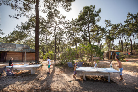Huéspedes del parque vacacional juegan al ping-pong entre pinos en Huttopia Lac de Carcans, Nouvelle-Aquitaine, Francia.
