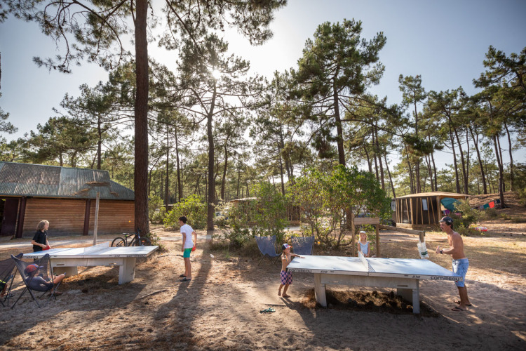 Holiday park guests play table tennis surrounded by pine trees at Huttopia Lac de Carcans in Nouvelle-Aquitaine, France.