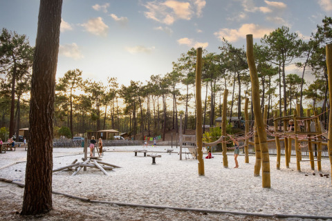 Niños juegan en un parque infantil de arena rodeado de pinos en Huttopia Lac de Carcans, Francia.