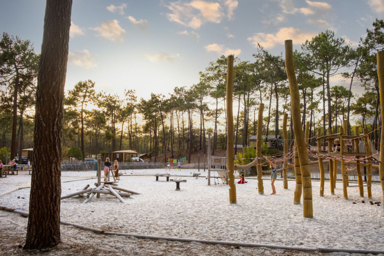 Kinderen spelen op een zandige natuurspeeltuin omringd door dennen bij Huttopia Lac de Carcans, Frankrijk.
