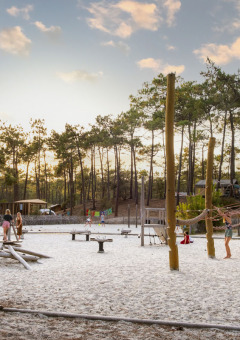 Kinder spielen auf einem naturbelassenen Spielplatz mit Sand, umgeben von Kiefern im Huttopia Lac de Carcans.