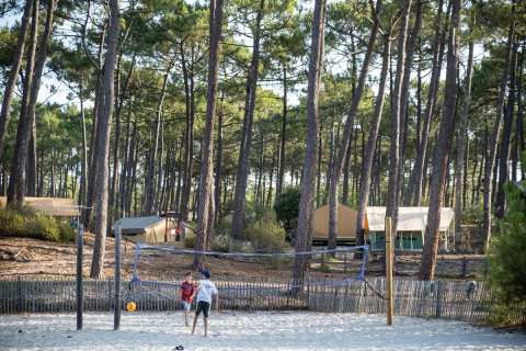 Niños juegan voleibol en la arena entre pinos y tiendas en Huttopia Lac de Carcans, Nueva Aquitania, Francia.