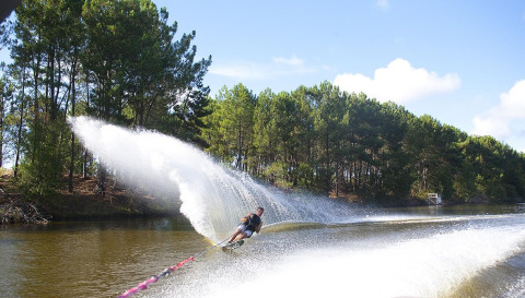 Waterskiër in volle actie op een kanaal nabij Carcans, omgeven door bomen en een stralende lucht.