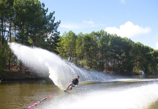 Water-skier creates a spray as they glide along a tree-lined canal near Carcans in Nouvelle-Aquitaine, France.