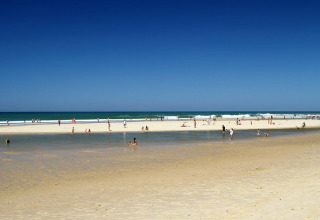 Strandbillede nær Carcans, Nouvelle-Aquitaine, Frankrig, med folk, der nyder solen og det klare vand.