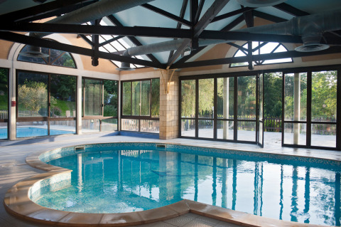 Indendørs swimmingpool med store vinduer og udsigt til haven på Huttopia Sarlat, Nouvelle-Aquitaine, Frankrig.