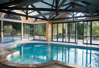 Indendørs swimmingpool med store vinduer og udsigt til haven på Huttopia Sarlat, Nouvelle-Aquitaine, Frankrig.