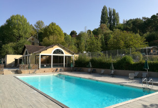 Piscine extérieure au village vacances Huttopia Sarlat en Nouvelle-Aquitaine, France, entourée de verdure.