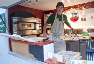 En pizzabager i en foodtruck laver pizza til gæster på Huttopia Sarlat ferieparken i Nouvelle-Aquitaine, Frankrig.