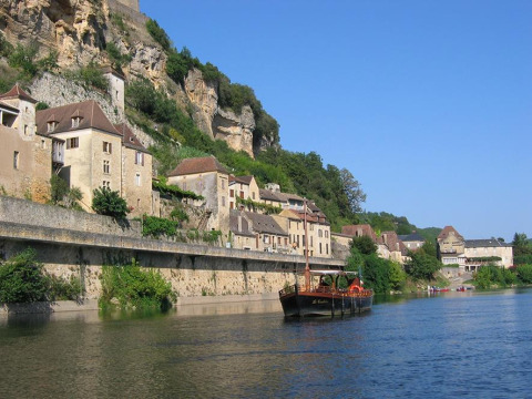 Barco en el río junto a casas en acantilado cerca de Huttopia Sarlat, Nouvelle-Aquitaine, Francia.