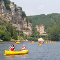 Personas reman en canoas amarillas por un río cerca de Sarlat la Caneda, con castillo y acantilados verdes.