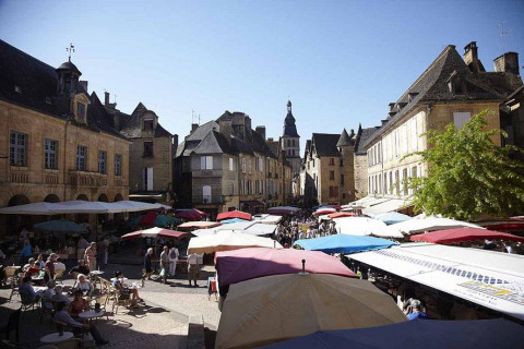 Scène de marché avec des parasols colorés et des bâtiments historiques à Huttopia Sarlat, Nouvelle-Aquitaine.