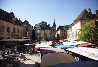 Scène de marché avec des parasols colorés et des bâtiments historiques à Huttopia Sarlat, Nouvelle-Aquitaine.