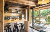 Lyst køkken og spiseområde i Chalet Portland, åbner ud til en terrasse med udsigt til grøn natur.