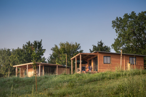 Twee houten chalets, waaronder Chalet Ottawa, op een grasheuvel met bomen en een heldere lucht eromheen.