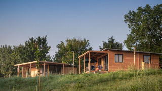 To træhytter, herunder Chalet Ottawa, står på en grøn bakke omgivet af træer under en klar himmel.