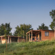 To træhytter, herunder Chalet Ottawa, står på en grøn bakke omgivet af træer under en klar himmel.